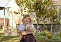 Woman in garden holding a cat, enjoying a sunny day. Relaxed and joyful moment outdoors.