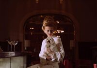 A sophisticated woman in a classic bar setting holding a Maltese dog.