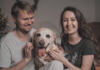 Happy couple playing with their Labrador dog at home, showcasing love and companionship.