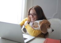 A happy woman using a laptop at home, hugging her beagle dog while enjoying remote work.